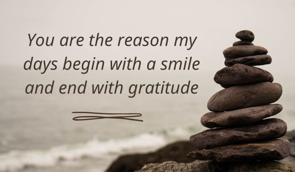 Serene coastal landscape background featuring a stack of balanced rocks in cairn formation, highlighting thoughtful good morning messages for her: "You are the reason my days begin with a smile and end with gratitude".